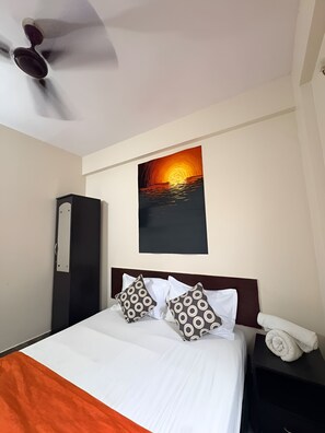 A hotel room with a bed, a painting, a wardrobe, and a nightstand. - MALABAR INN (Bengaluru)