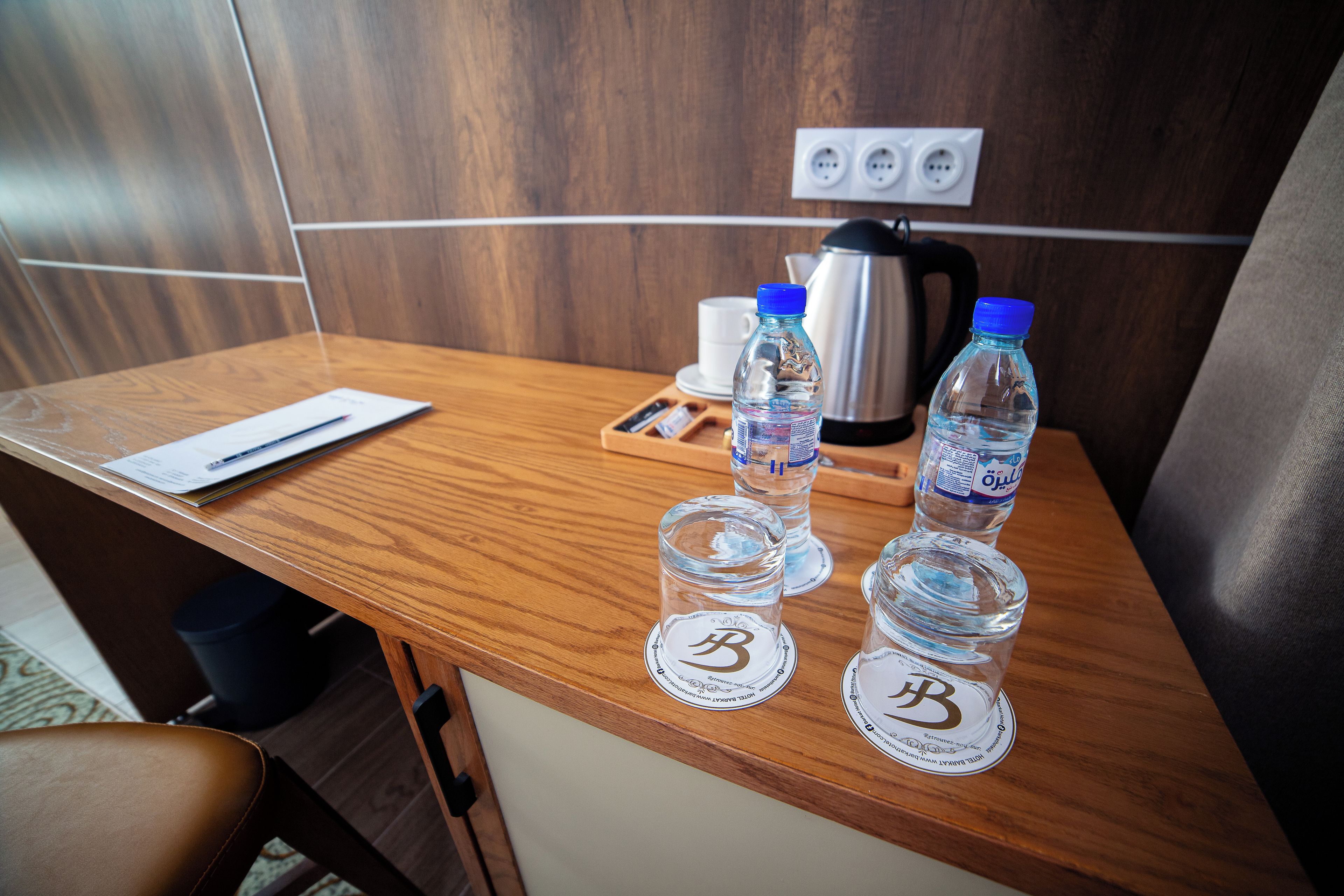 Un escritorio de madera con una computadora portátil, dos botellas de agua y un hervidor.