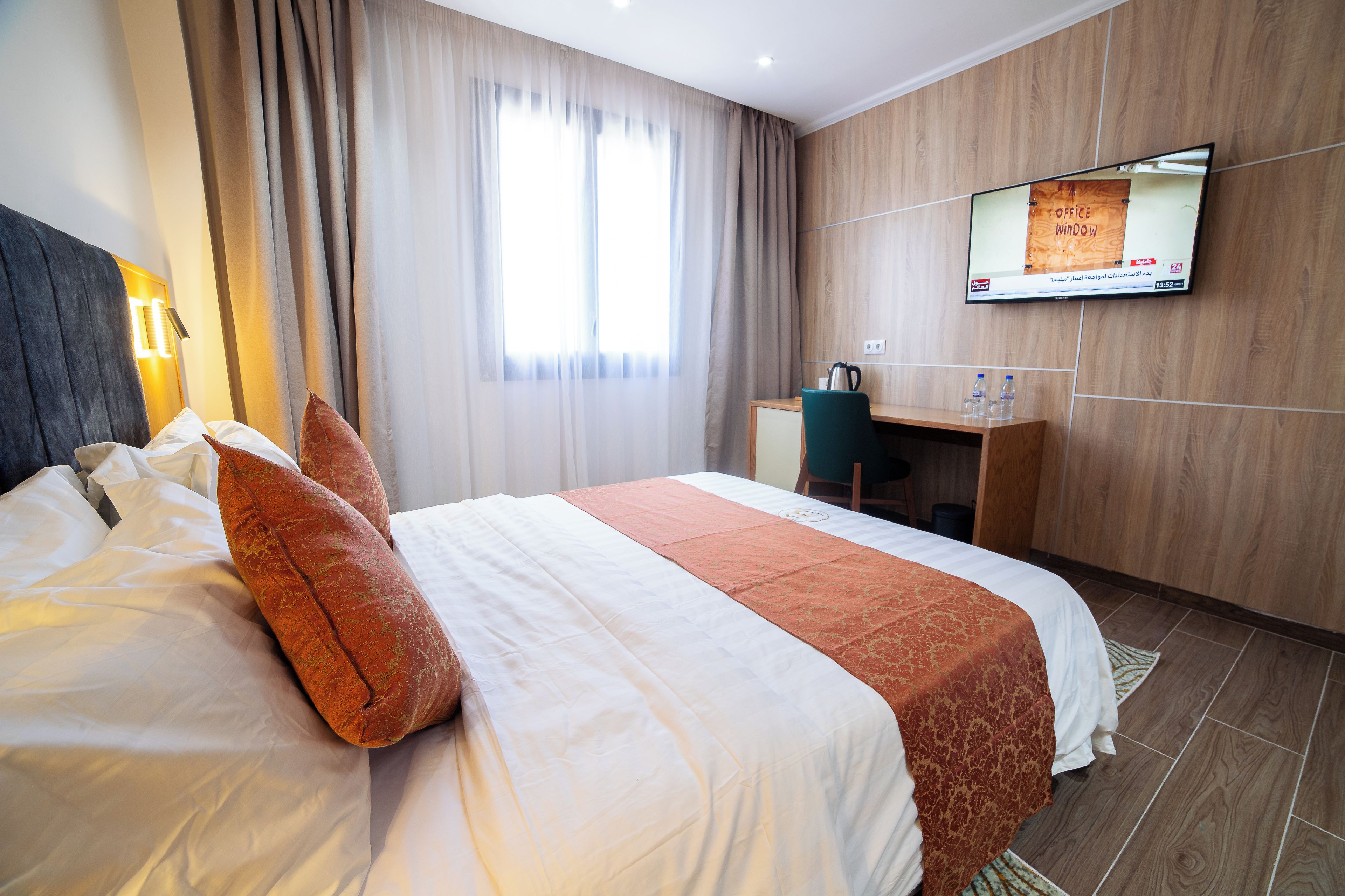 A hotel room with a bed, a desk, a television, and a window with curtains.