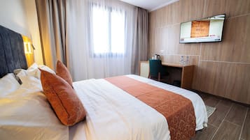 A hotel room with a bed, a desk, a television, and a window with curtains.
