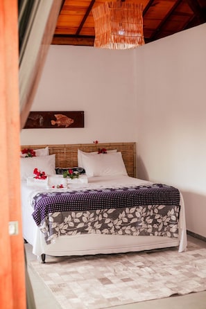 Una cama bien hecha con una colcha estampada, cabecera de madera y una lámpara colgante.