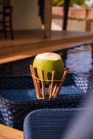 Un coco verde en una cesta tejida sobre una silla junto a una piscina.