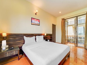A hotel room with a large bed, bedside lamps, a telephone, a painting on the wall, and a balcony with curtains. - Deluxe Aveeno Villas (Saligao)