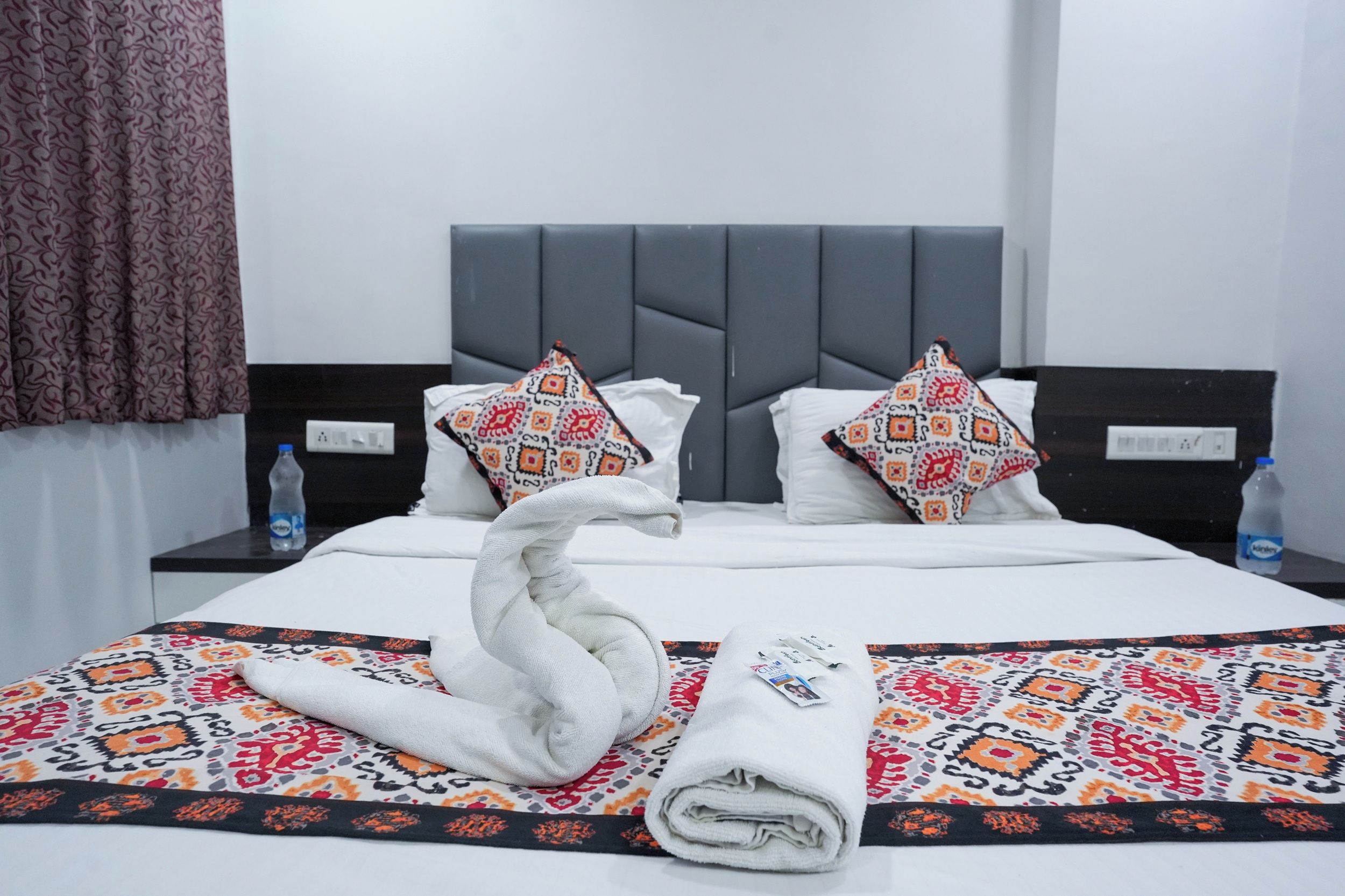 A hotel room with a bed, two pillows, a water bottle, and a towel.