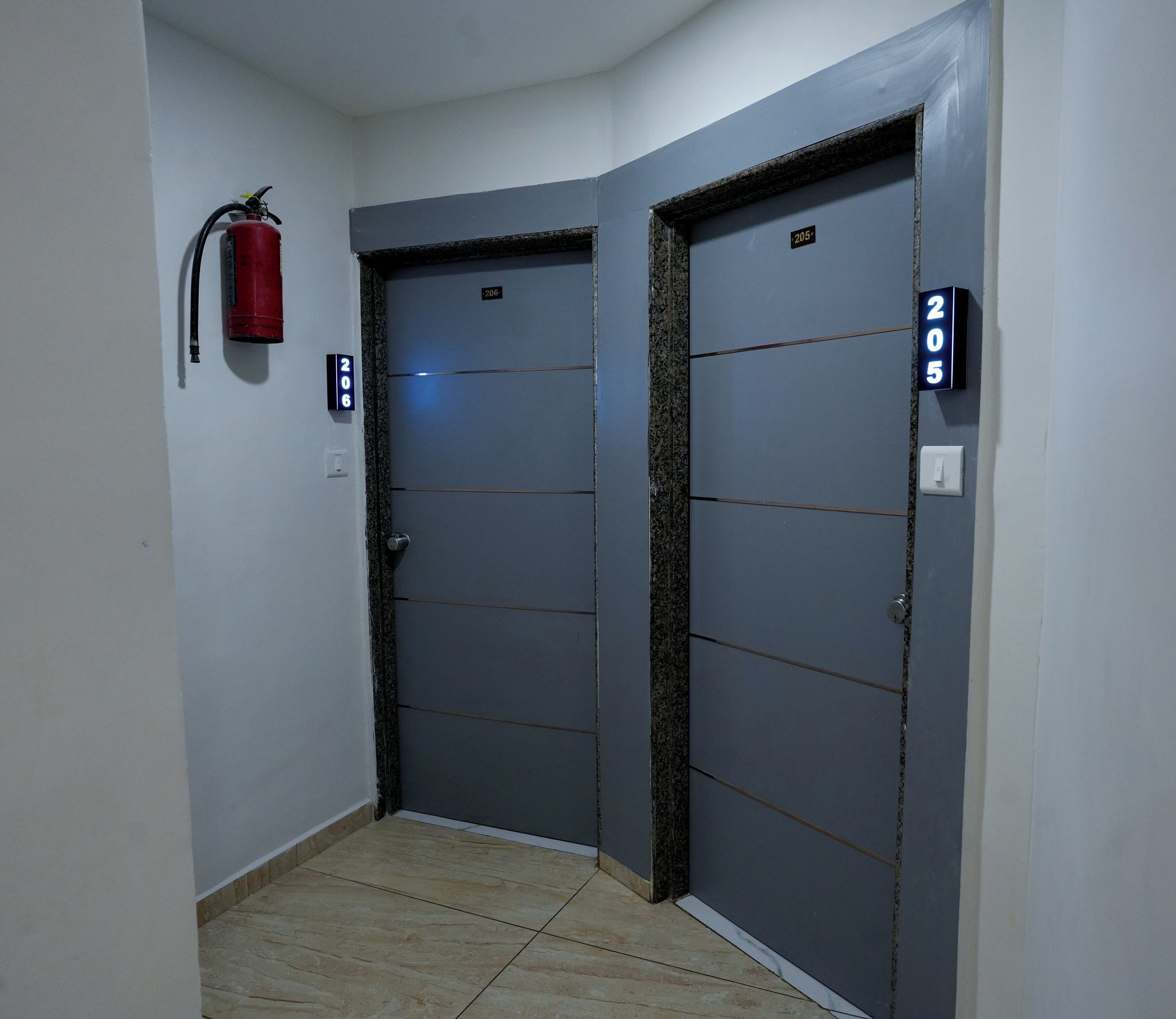 A hallway with two doors, each marked with a number. A fire extinguisher is mounted on the wall to the left.