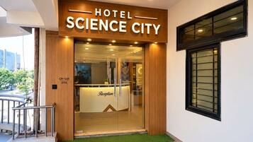 A hotel entrance with a reception desk, a wooden facade, and a window with blinds.