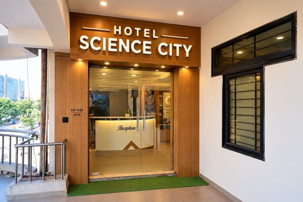 Entrada de hotel con mostrador de recepción, fachada de madera y ventana con persianas.