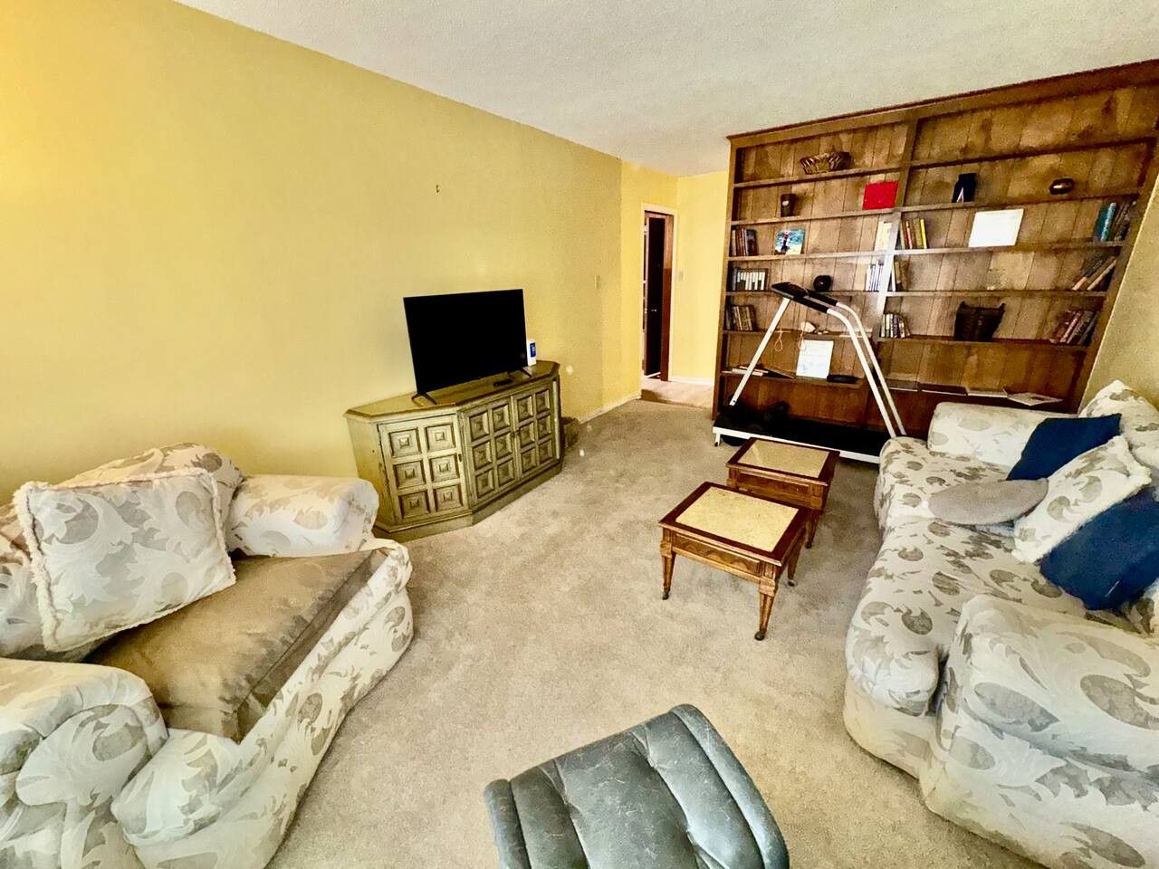A living room with a sofa set, a coffee table, a television, and a bookshelf.