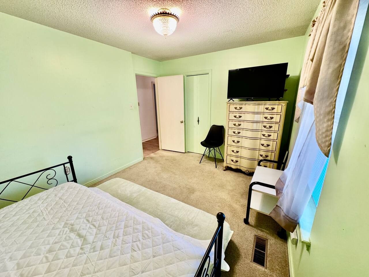 A bedroom with a bed, dresser, chair, and a television.