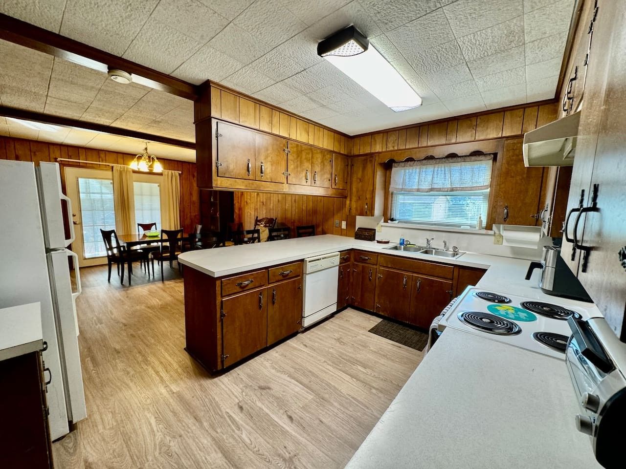 Une cuisine avec des meubles de rangement en bois, un plan de travail blanc, une cuisinière et un lave-vaisselle.