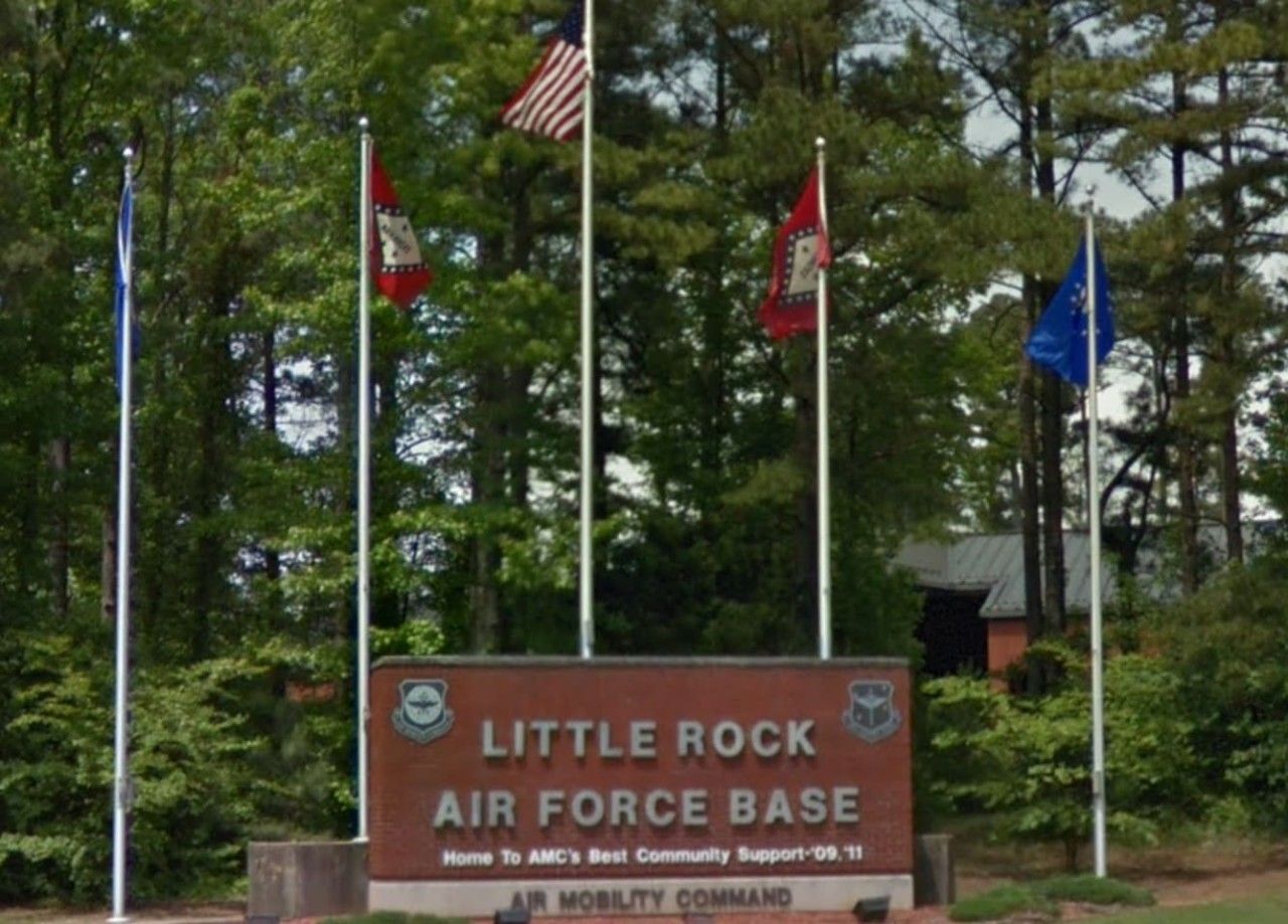 Schild für die Little Rock Air Force Base, mit Flaggen und einem Gebäude im Hintergrund.