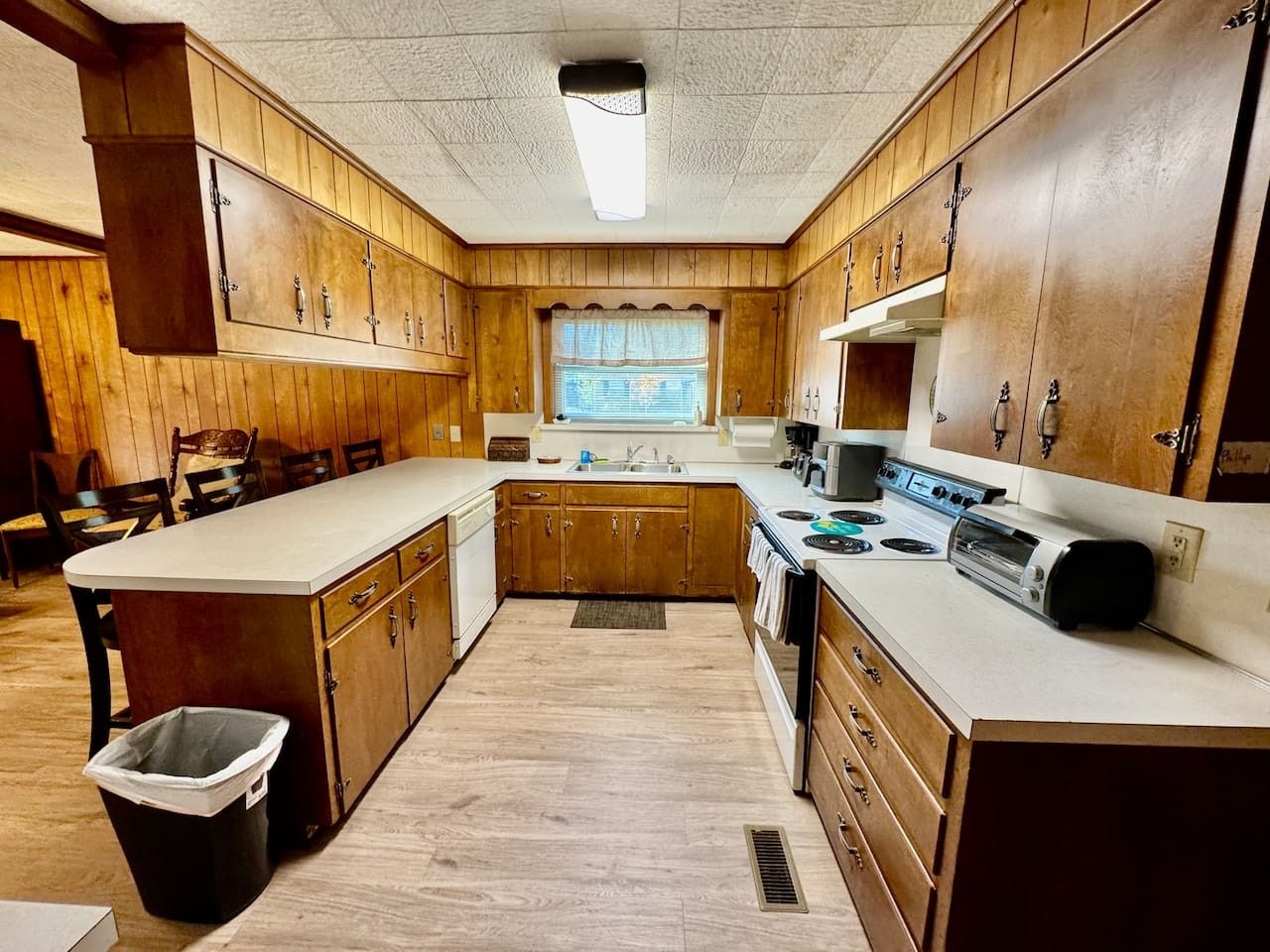 A kitchen with wooden cabinets, a central island, a stove, and a trash can.
