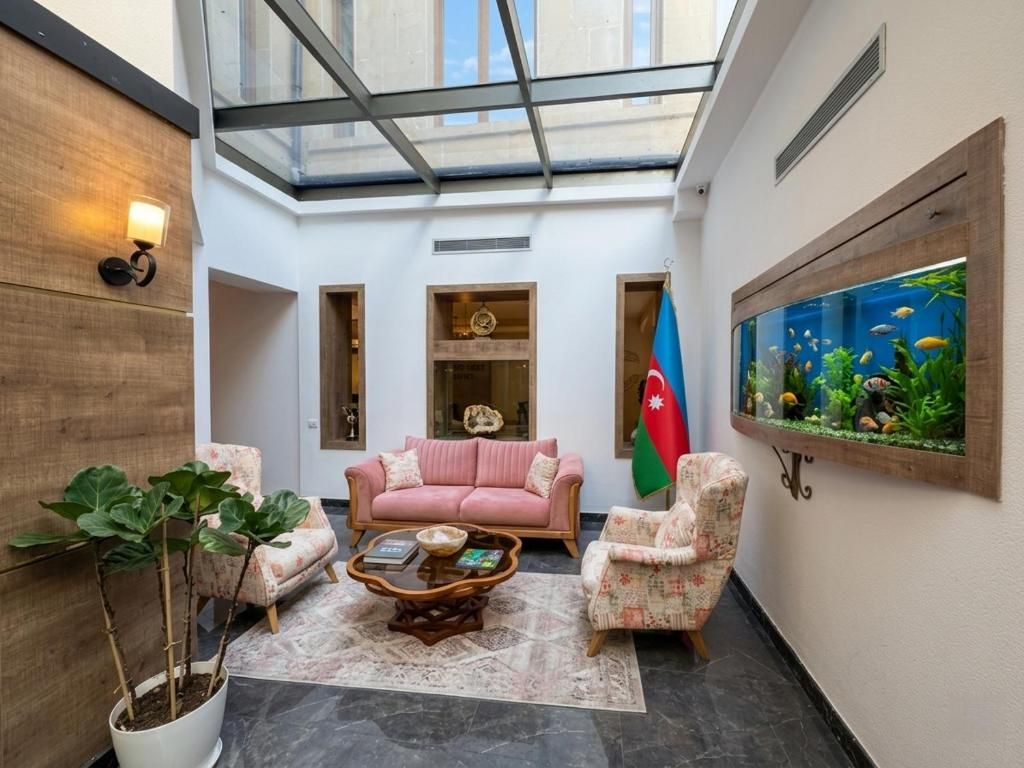 Una habitación con techo de vidrio, un sofá rosa, dos sillones, una mesa de centro, una bandera y un acuario.