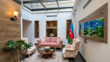 Una habitación con techo de vidrio, un sofá rosa, dos sillones, una mesa de centro, una bandera y un acuario.