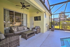 A covered patio area with wicker furniture, a ceiling fan, a pool, and a television. - Windsor Palms Escape | Private Pool & Game Room (Kissimmee)
