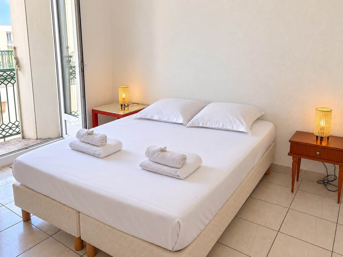 Une chambre d’hôtel avec un grand lit, deux tables de chevet et un balcon avec vue.