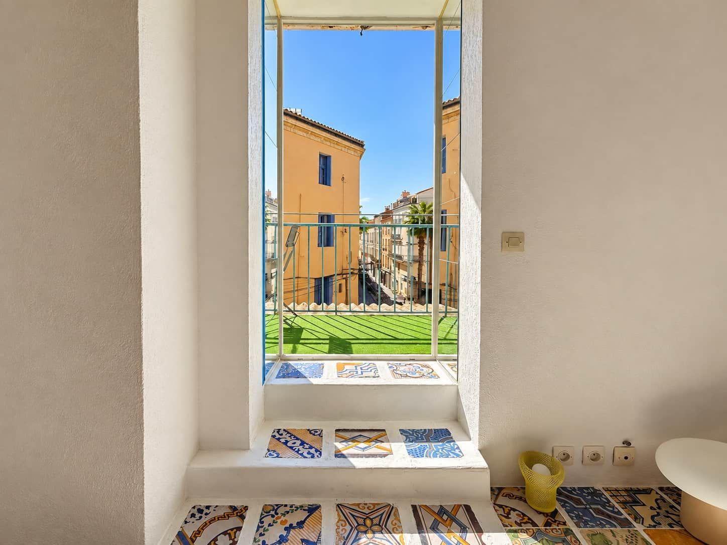 A bathroom with a window overlooking a courtyard with a tiled floor and a building in the background.