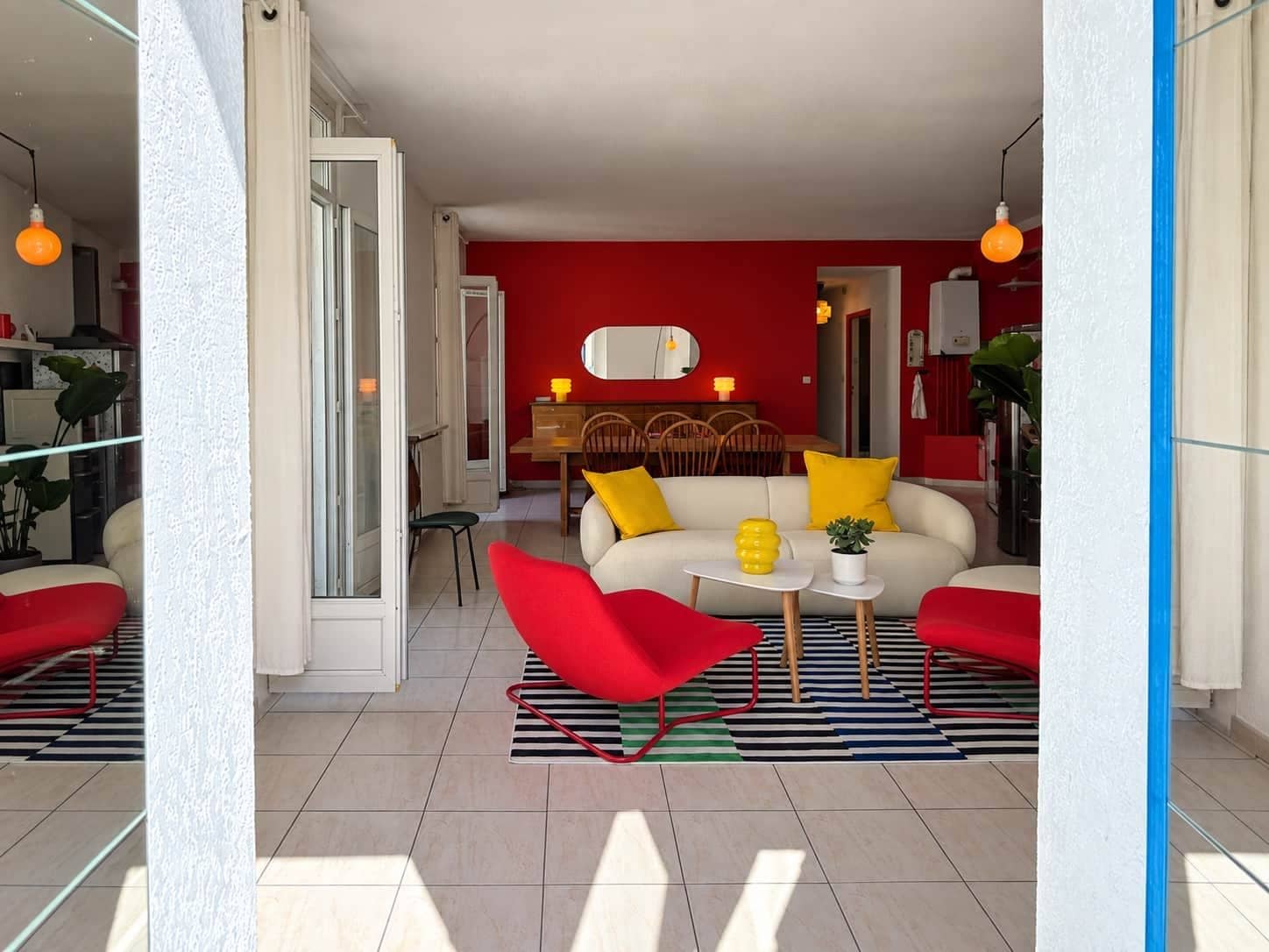 Een moderne woonkamer met een rode bank, een rode fauteuil en een gestreept vloerkleed.