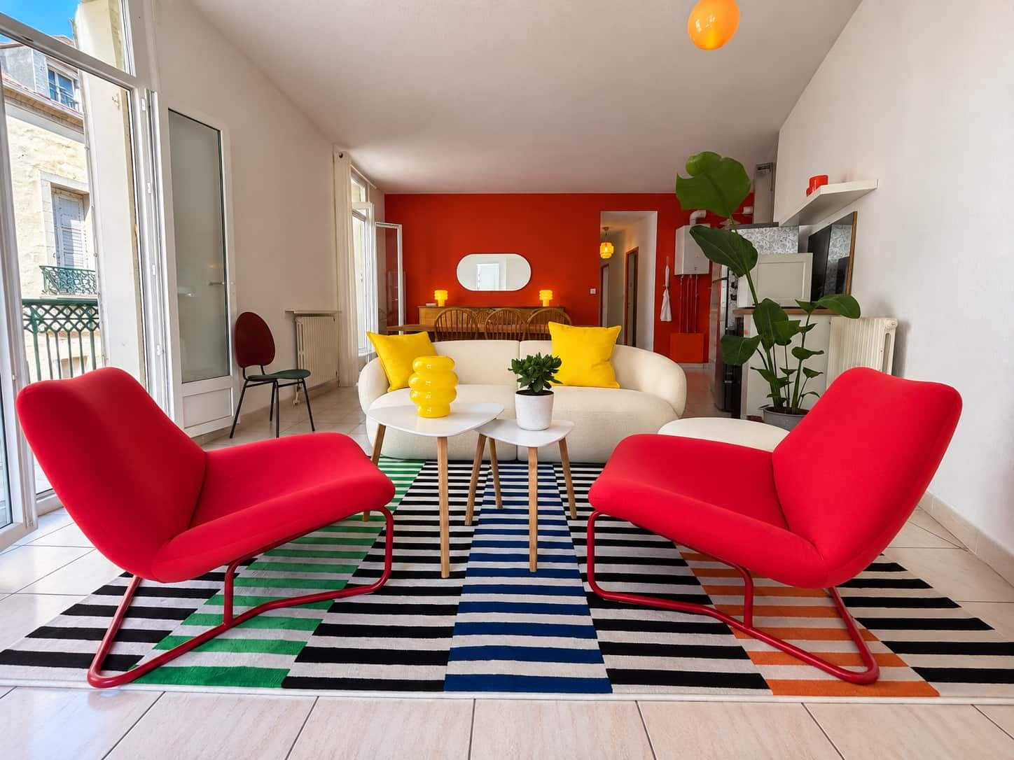 Un salon moderne avec un canapé, deux fauteuils rouges, une table basse et un tapis à rayures.