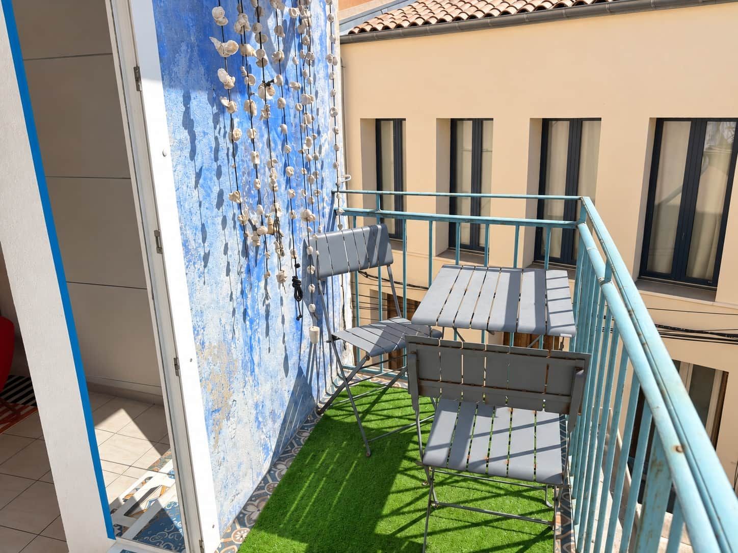Un balcon avec un revêtement de sol en gazon synthétique, une rambarde en métal et un mur orné de décorations suspendues.