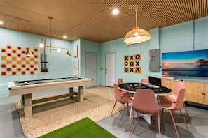 Een kamer met een pooltafel, een tafeltennistafel en een biljarttafel. Er staan vier roze stoelen rond een tafel met een spel.