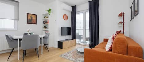 A modern living room with a sofa, a dining table with chairs, a TV, and a large window with curtains.