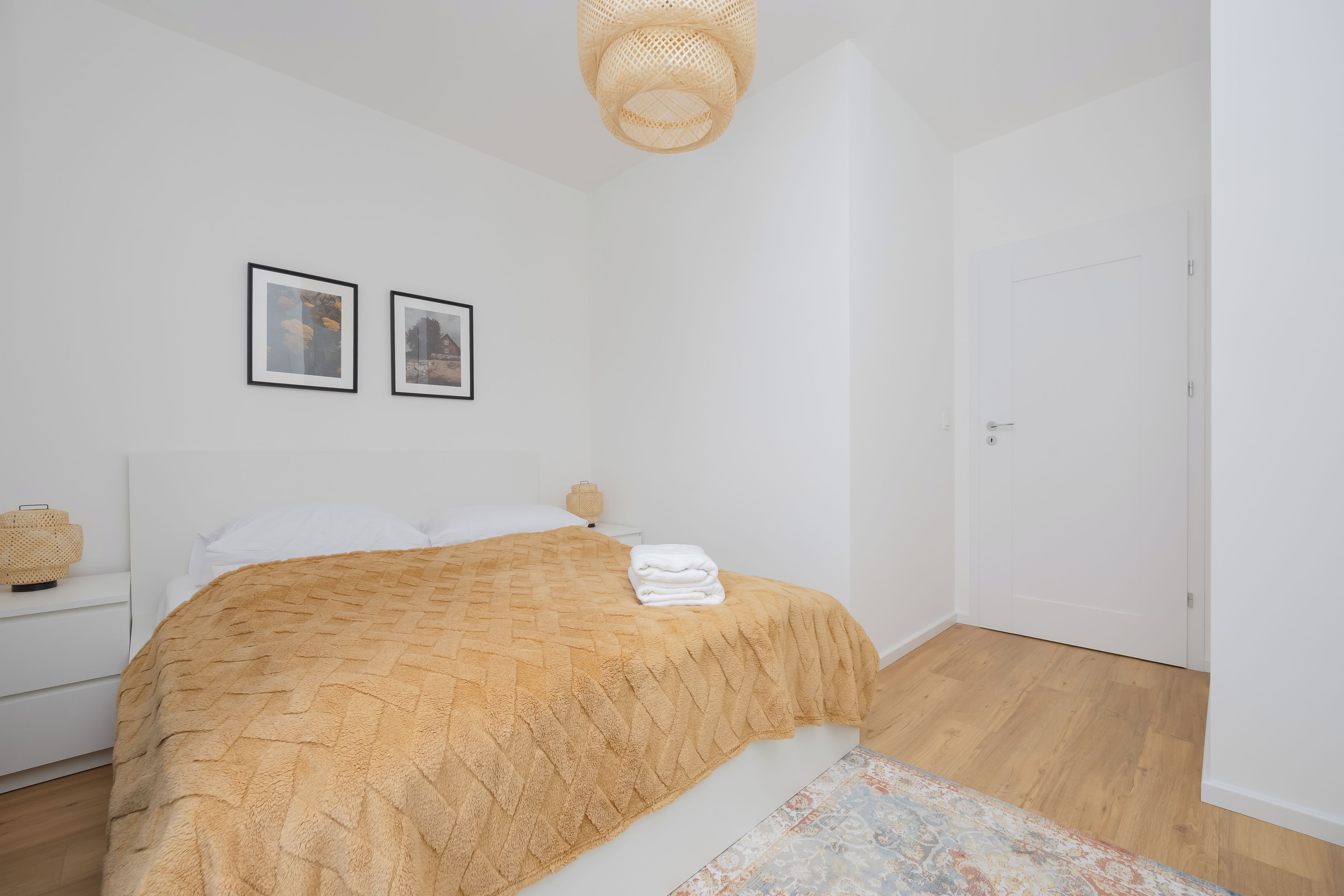 Une chambre à coucher avec un lit, deux tableaux encadrés au mur, une lampe de chevet et une porte.