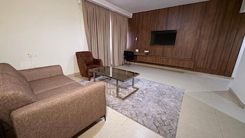 Un salon comprenant un canapé, une table basse, un téléviseur fixé au mur et un tapis à motifs.