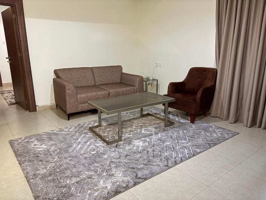 A living room with a sofa, armchair, and coffee table on a patterned rug.