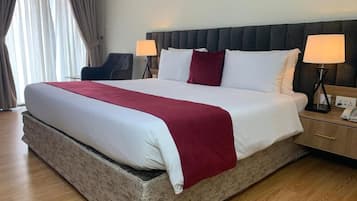 Una habitación de hotel con una cama grande, dos lámparas de noche, un cabecero y una ventana con cortinas.