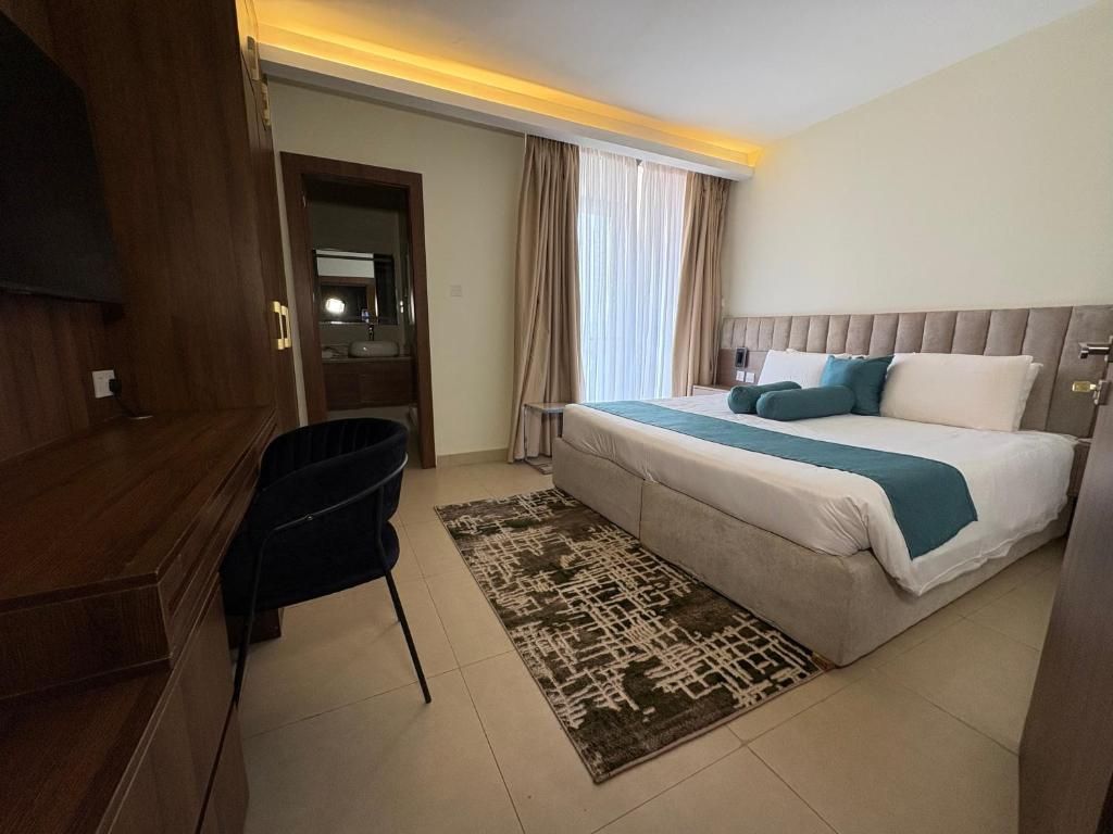 Habitación de hotel con cama, escritorio, silla, televisor y ventana con cortinas.