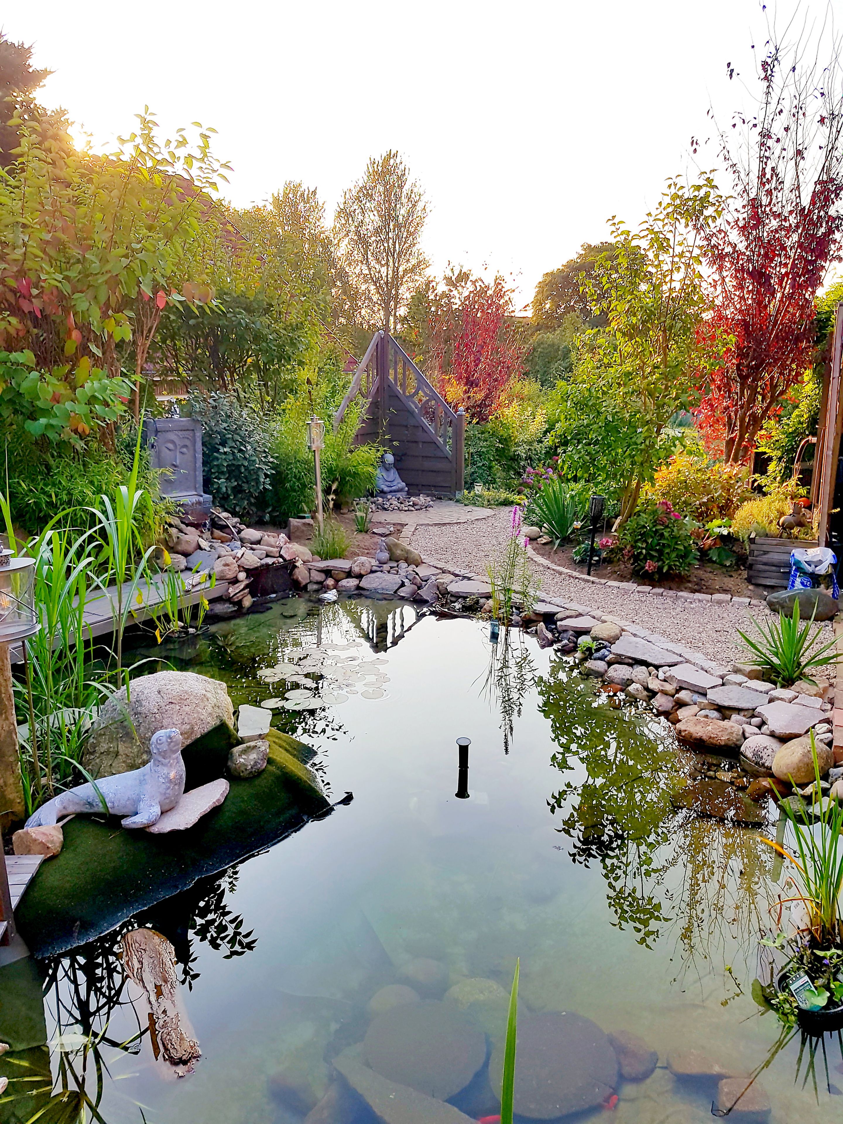 A tranquil garden with a pond, a wooden bridge, and a statue.