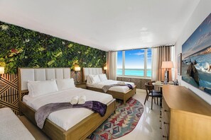 A hotel room with two beds, a large window with a view of the ocean, a wall with a green leafy design, and a painting of a beach scene. - Panoramic Ocean View Studio | Direct Beach Access (Miami Beach)