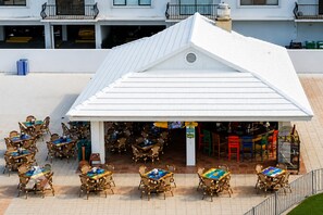 A covered outdoor seating area with tables and chairs, a bar, and a view of the building's exterior. - Panoramic Ocean View Studio | Direct Beach Access (Miami Beach)