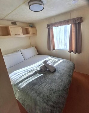 Een hotelkamer met een bed, een raam met gordijnen, een plafondlamp en ingebouwde planken boven het bed.