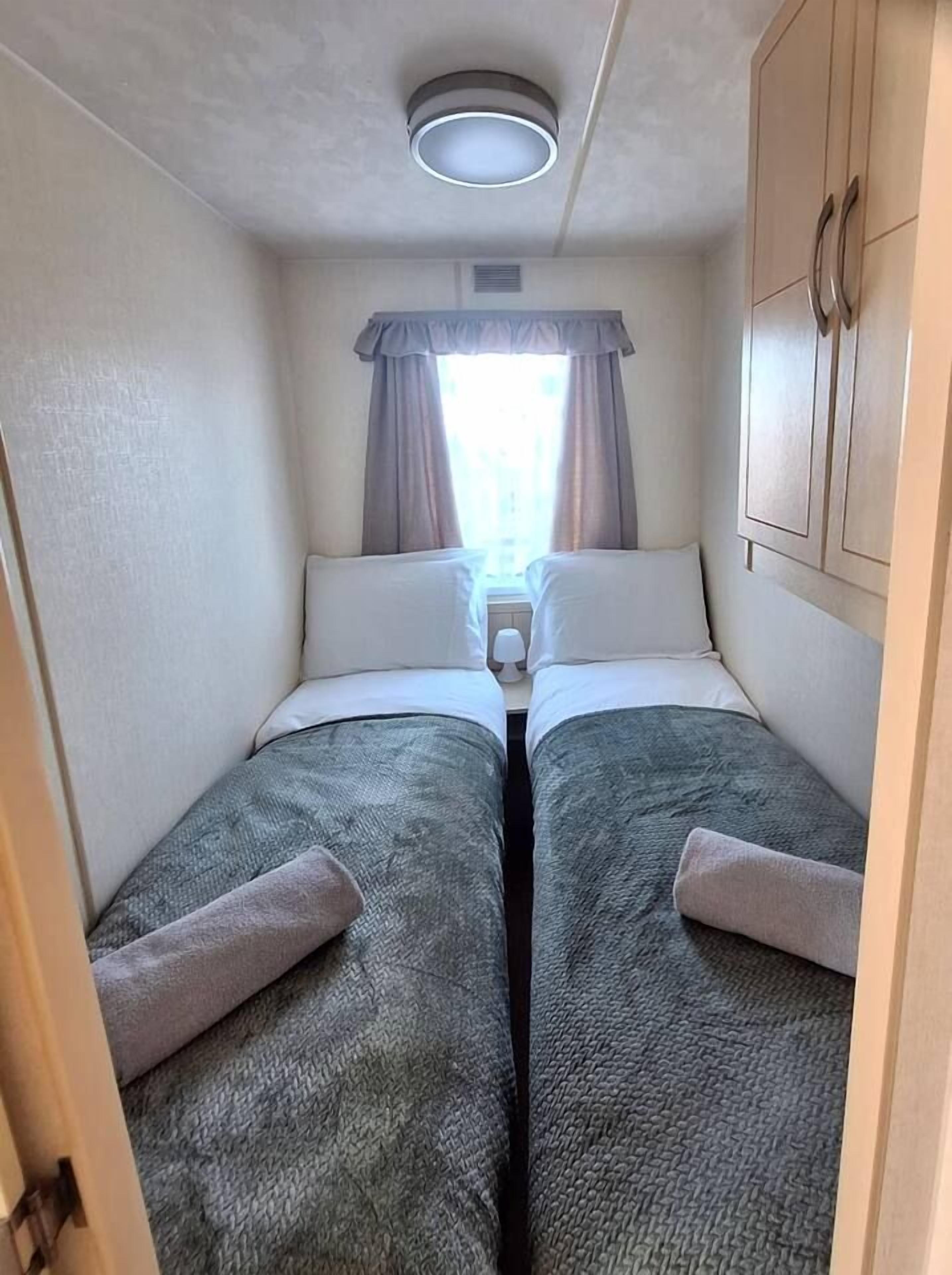 A narrow room with two beds, a window with curtains, a ceiling light, and a wardrobe.