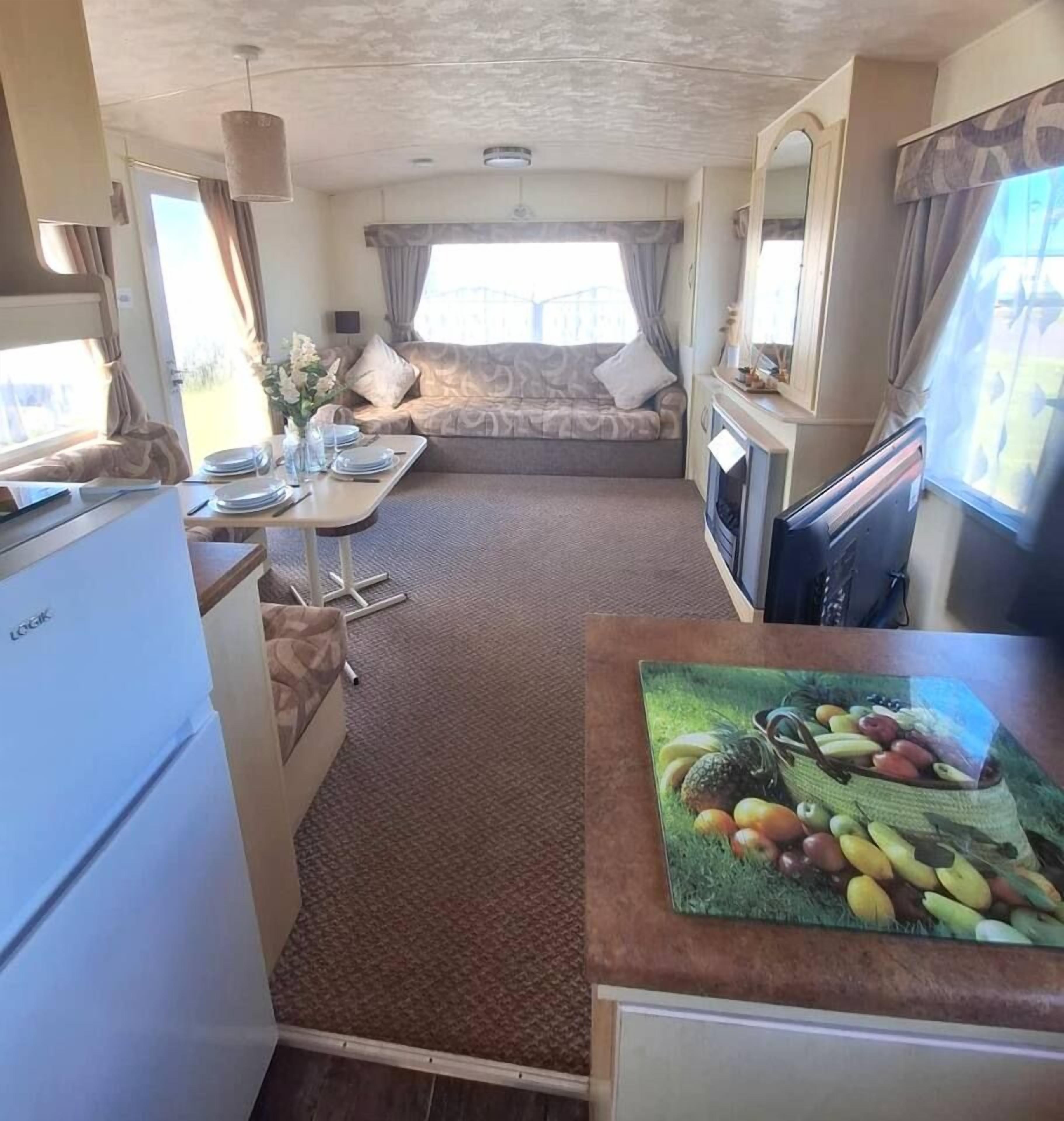 A compact RV interior with a kitchenette, dining area, and a bed.