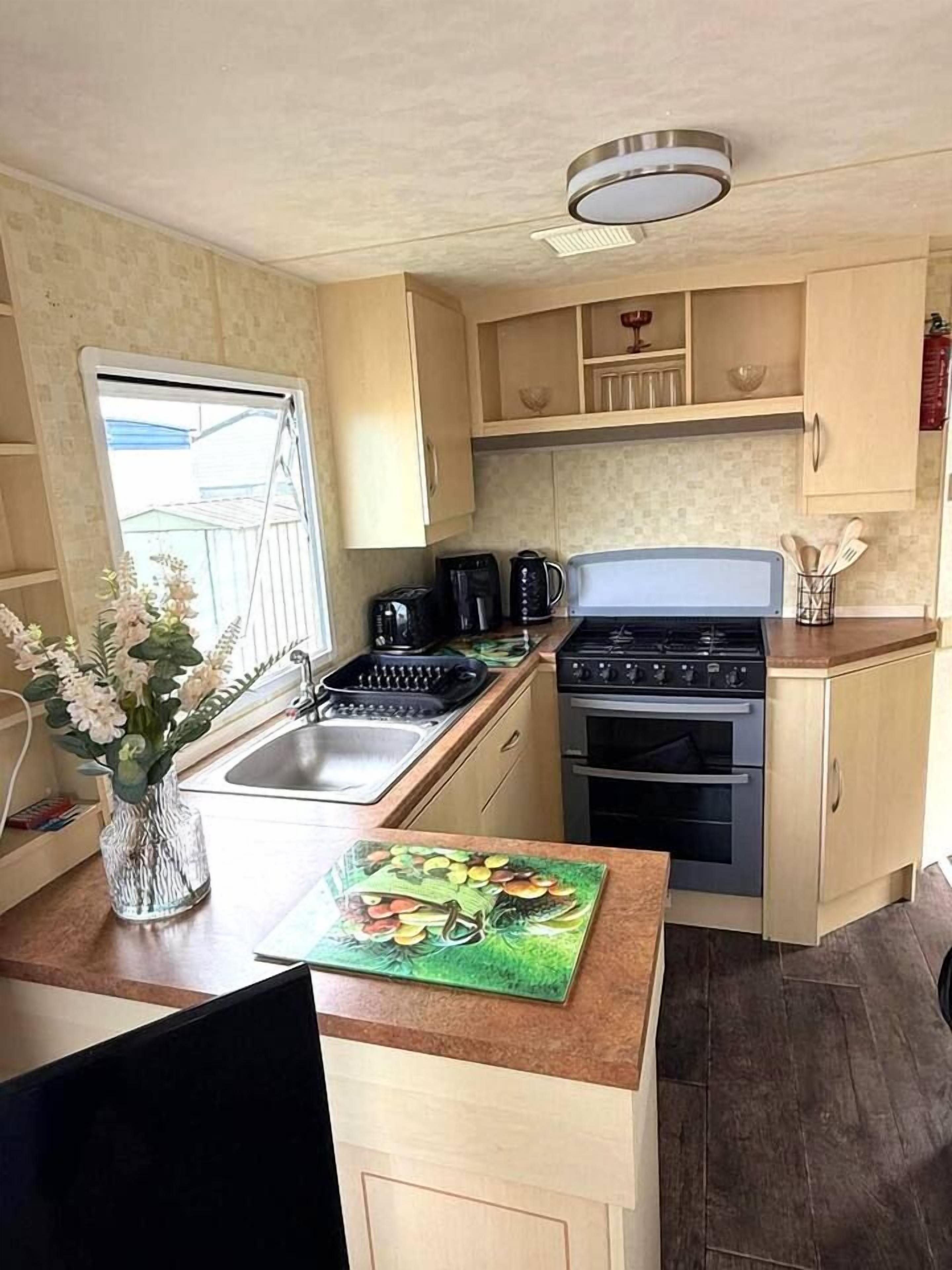 A compact kitchen with a gas stove, oven, and a sink. There is a window providing natural light and a decorative vase with flowers on the counter.
