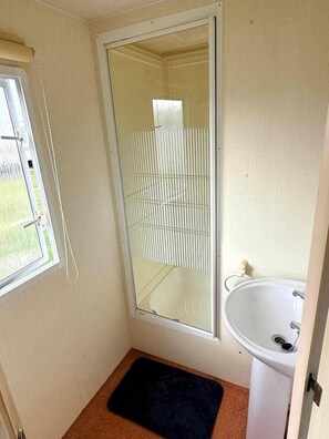 Een kleine badkamer met een raam, een wastafel en een zwarte mat.