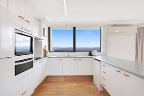A modern kitchen with white cabinets, a built-in oven, a large window with a view, and a wooden floor. - High-rise 2-bed Apartment in Surfers Paradise (Gold Coast)