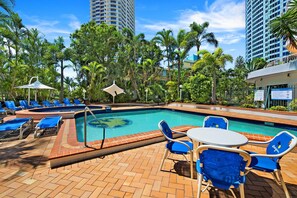 A pool area with lounge chairs and umbrellas, surrounded by palm trees and tall buildings. - High-rise 2-bed Apartment in Surfers Paradise (Gold Coast)