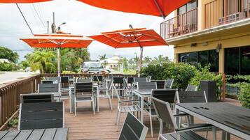 An outdoor patio with tables and chairs, covered by orange umbrellas, and a building with a balcony in the background.