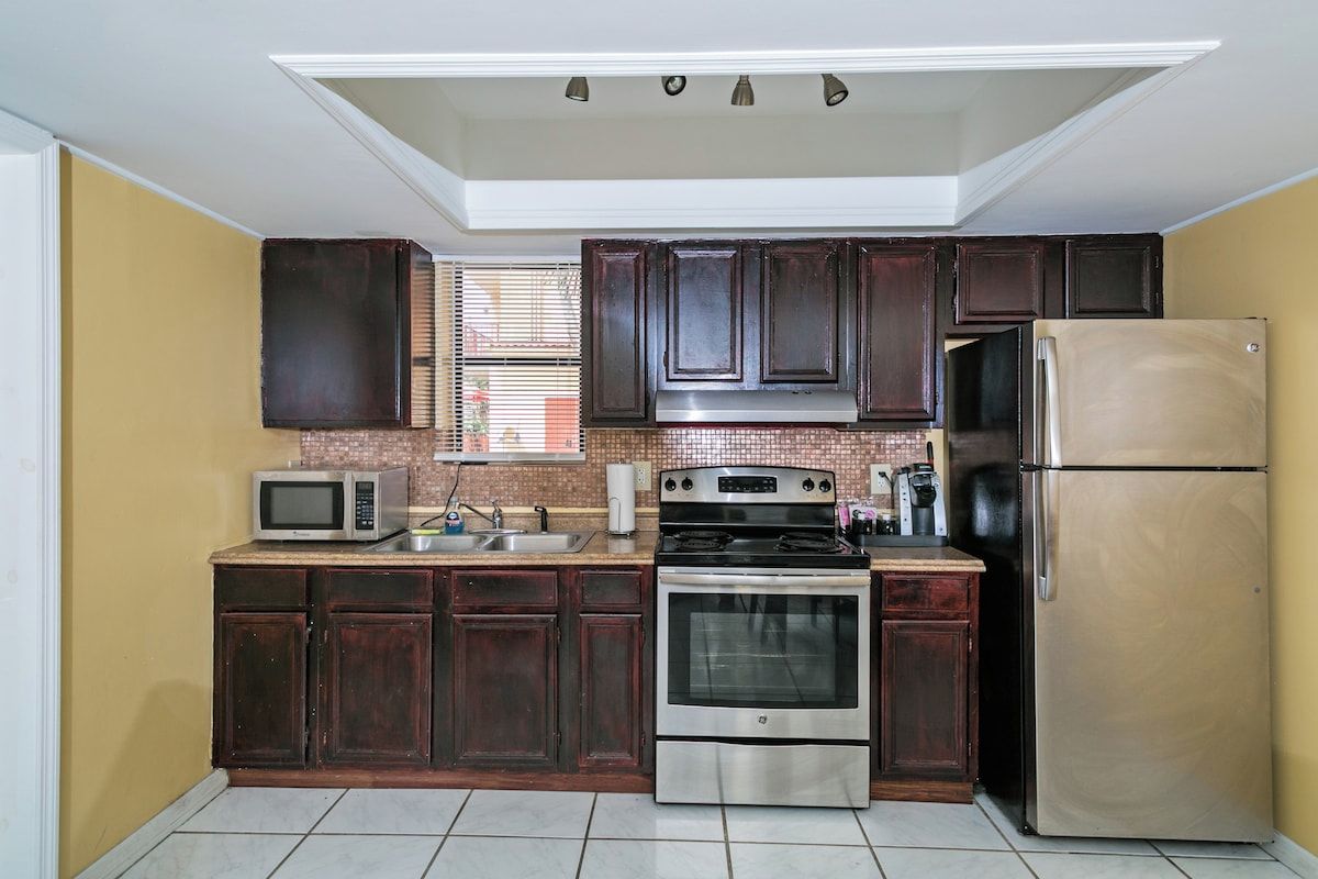 Una cocina con armarios de madera oscura, un refrigerador de acero inoxidable, un microondas, un horno y un lavamanos.