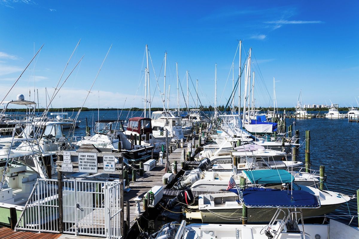 A marina with multiple boats docked, a wooden pier, and a clear blue sky.