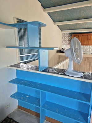 Een keuken met blauwe kastjes, een inbouwventilator en een raam met jaloezieën.