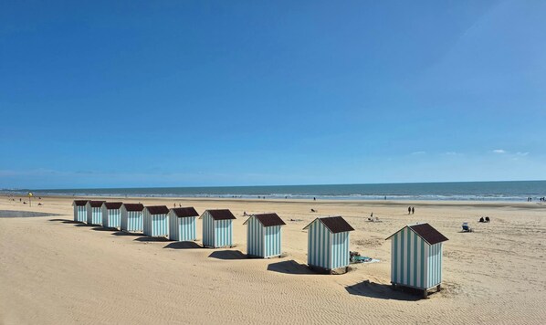 Een strand met een rij gestreepte strandhutten en een helderblauwe lucht.