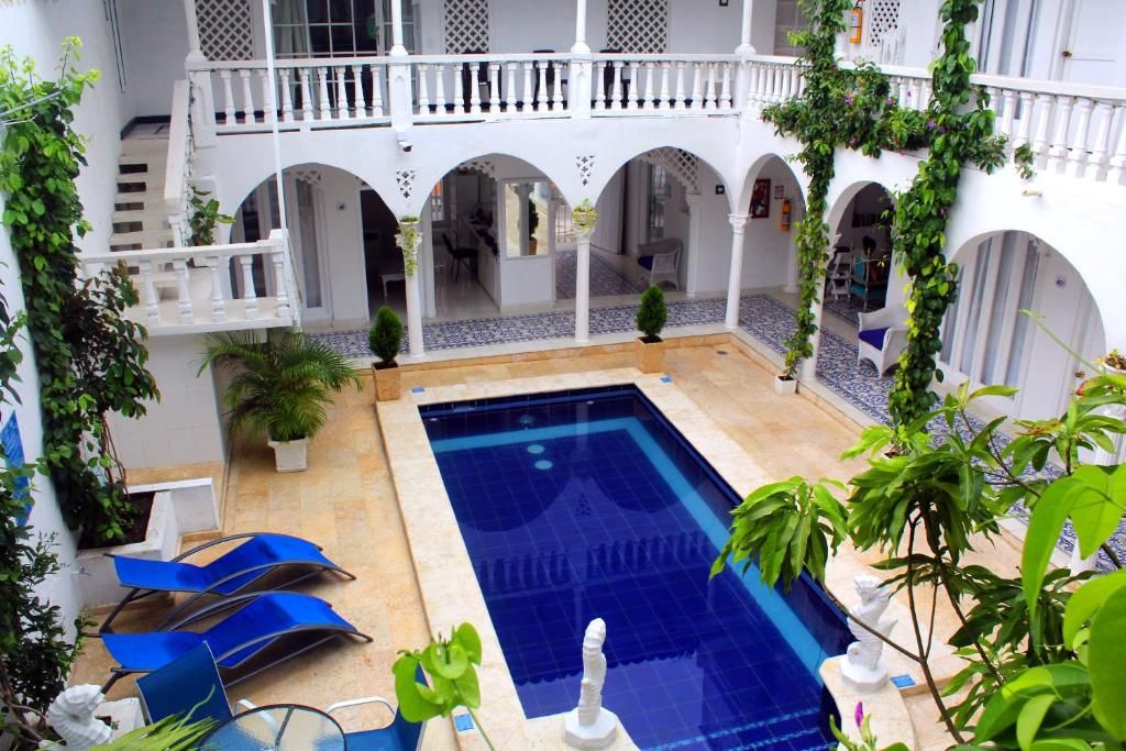 Un área de piscina con sillas reclinables azules, una estatua blanca y arcos.