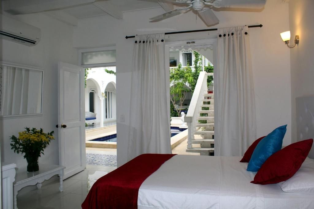 Une chambre d’hôtel avec un lit, des rideaux blancs, un ventilateur de plafond et une vue sur une piscine et un espace extérieur.