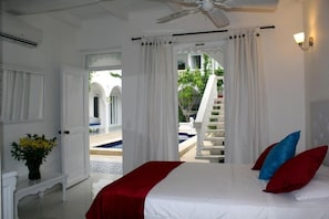 A hotel room with a bed, white curtains, a ceiling fan, and a view of a pool and outdoor area. - Hotel Casa Mara by Akel Hotels (Cartagena de Indias)