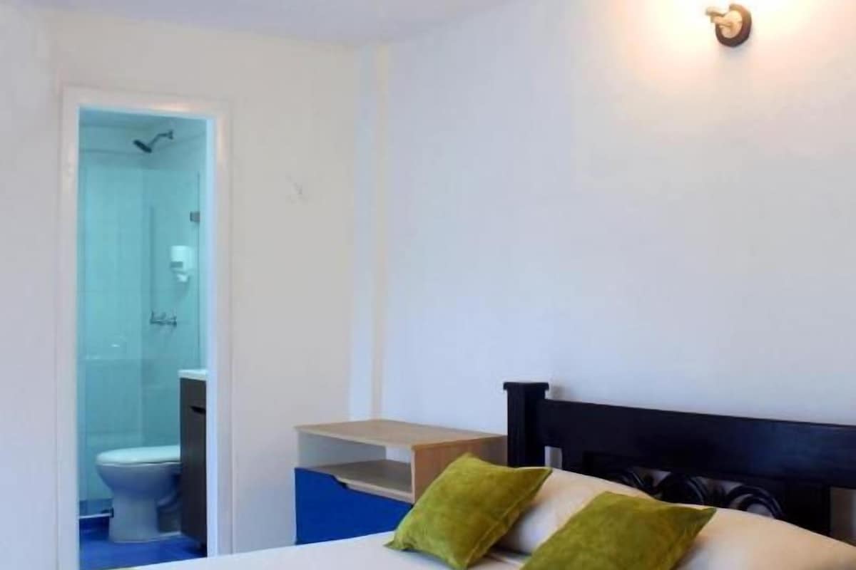 A hotel room with a bed, a nightstand, a wall-mounted light, and a bathroom visible through an open door.